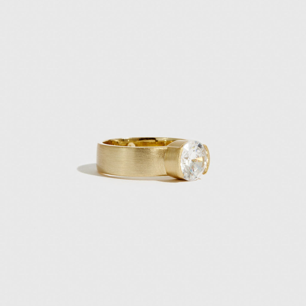 Gold ring with a clear gemstone on a light gray background